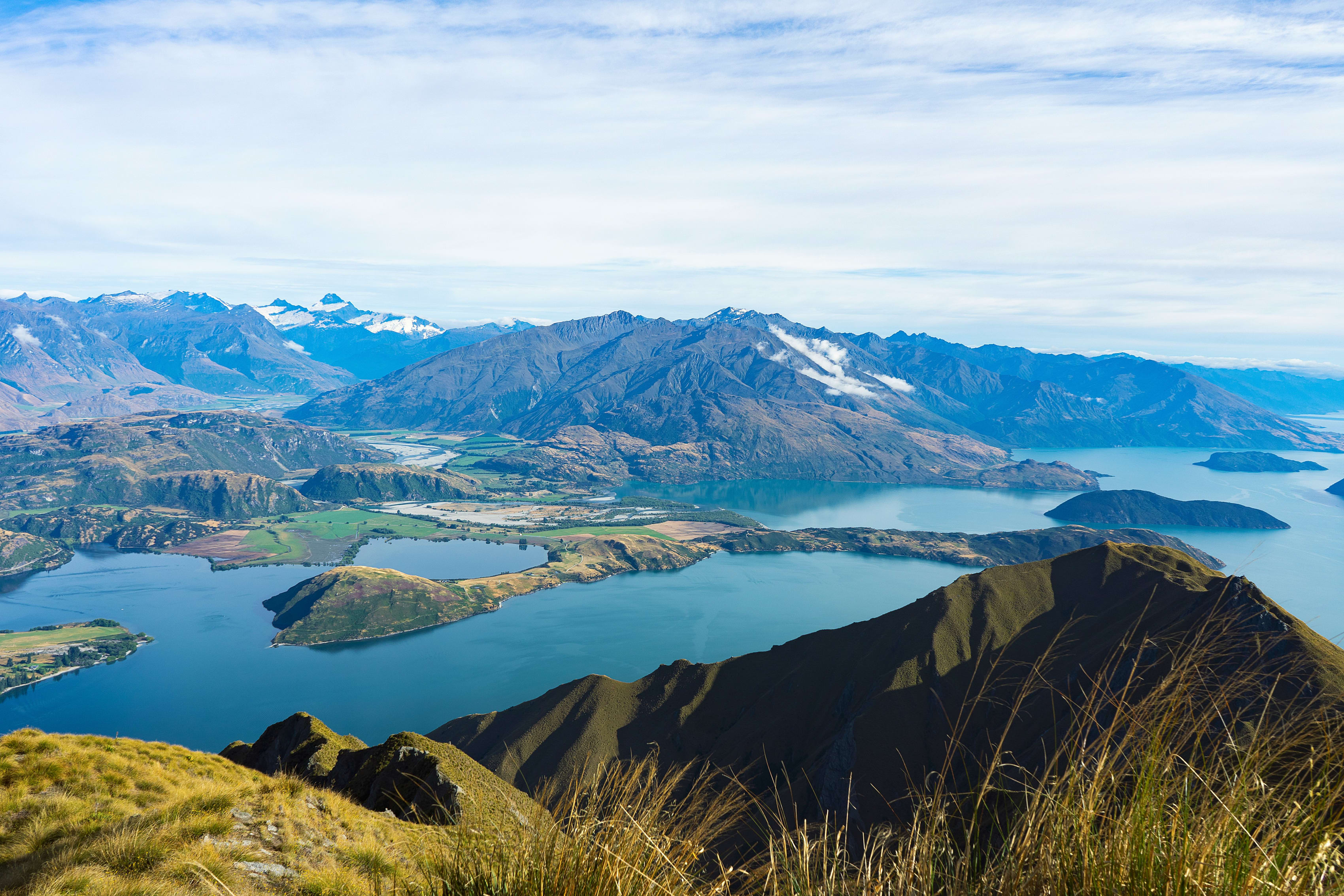 Aerial view of Lake Wanaka, New Zealand, surrounded by rugged mountains and lush islands under a clear sky.