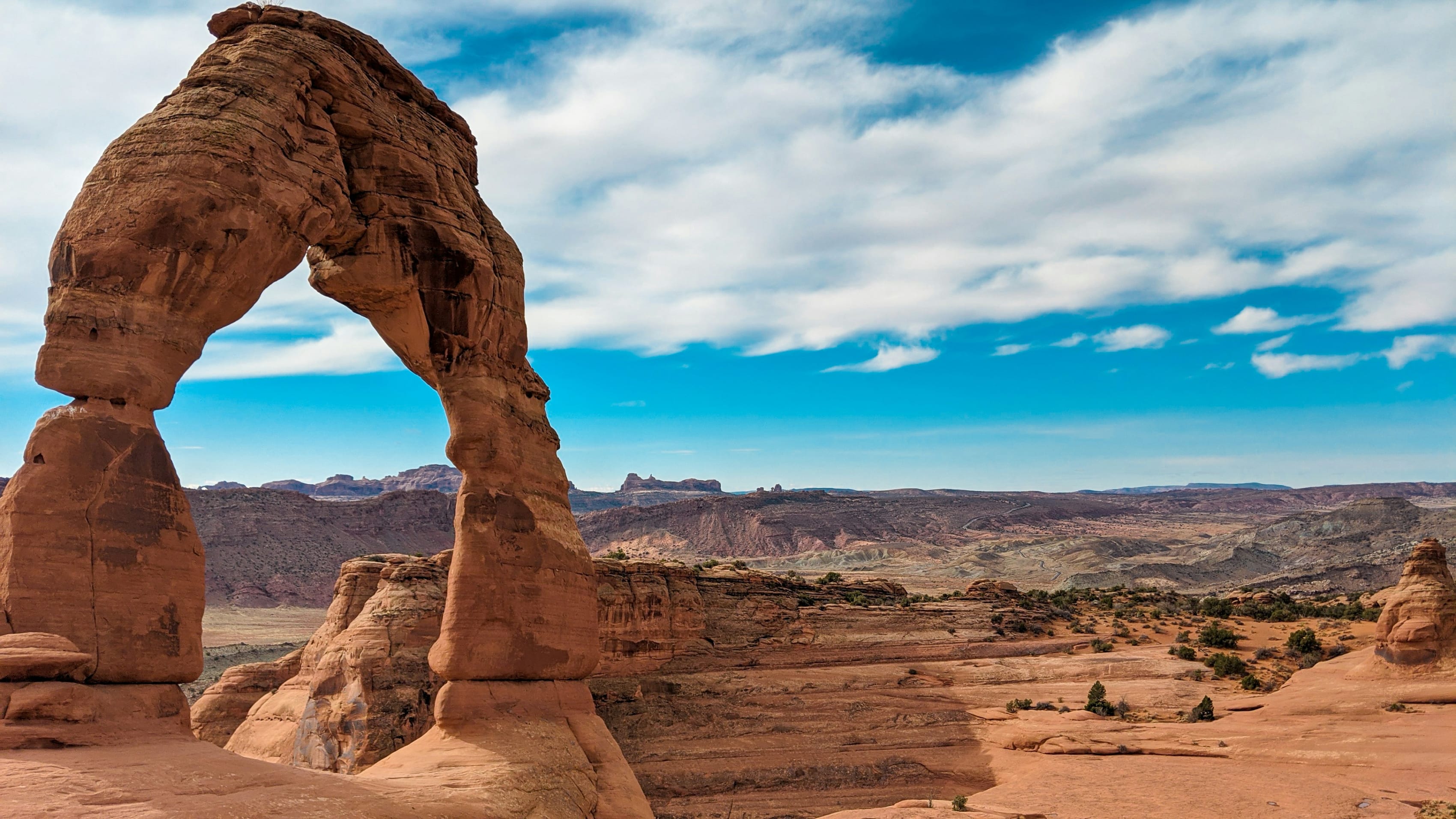 Delicate Arch in Arches National Park on a clear day with scattered clouds enhancing the vivid landscape.