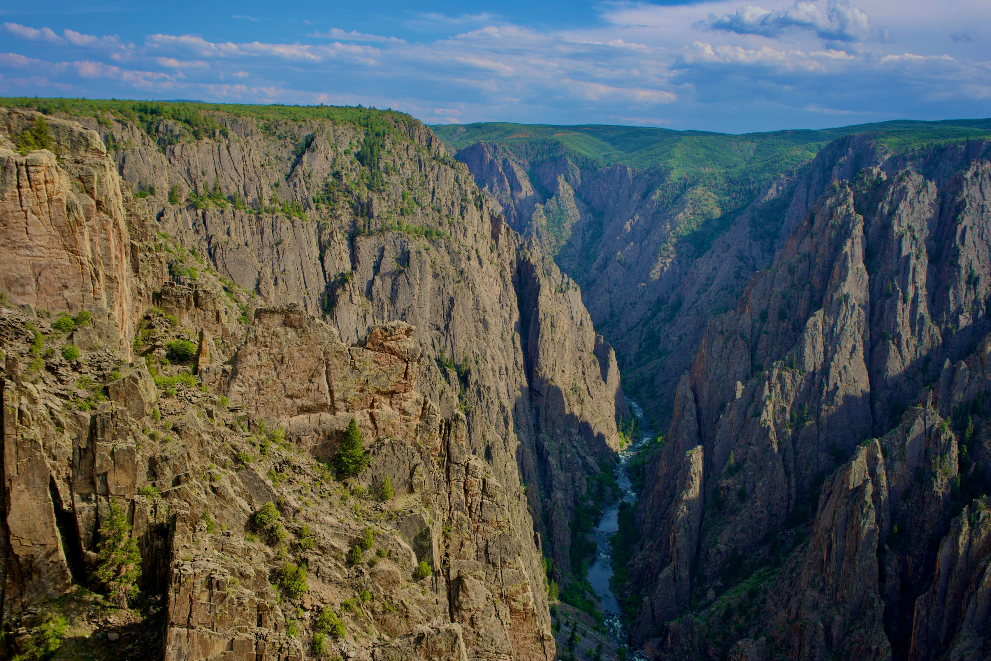 Aerial view of the deep Black Canyon of the Gunnison with steep cliff walls under a clear blue sky.