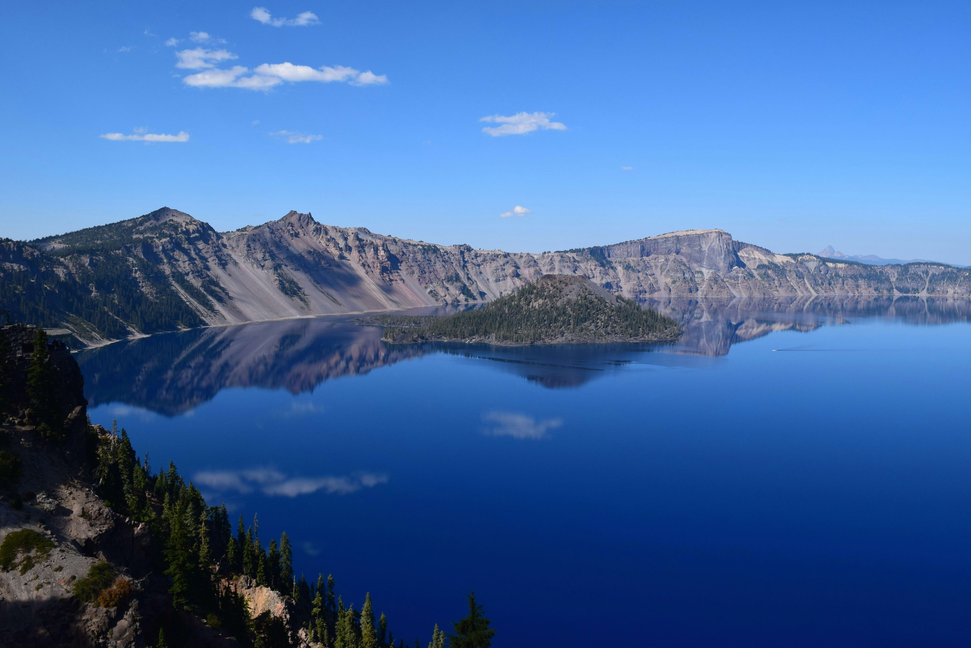 Scenic view of Crater Lake National Park with deep blue waters and surrounding cliffs reflecting on the surface.