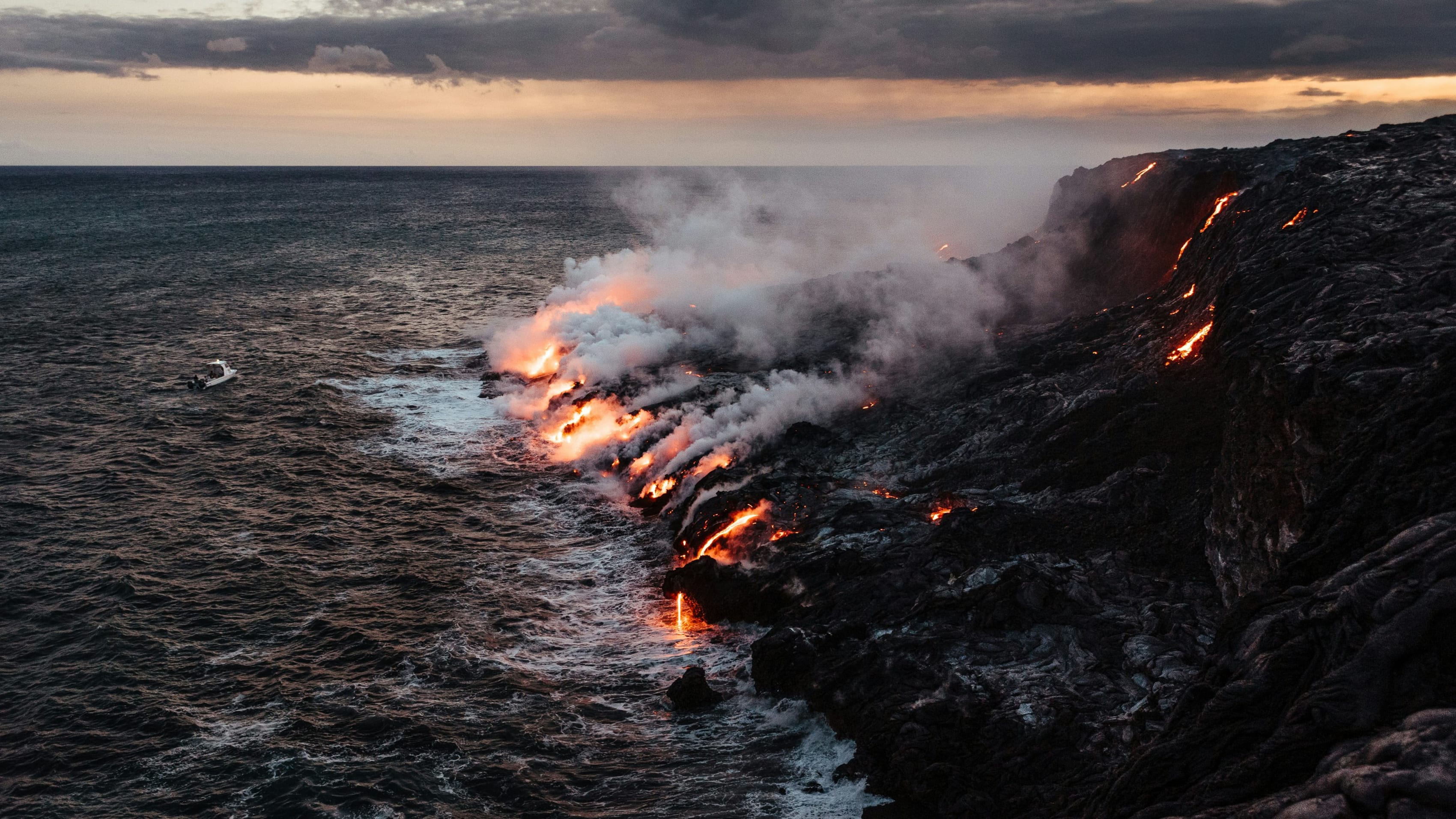 Hawaii Volcanoes National Park with molten lava flowing into the ocean at dusk creating steam