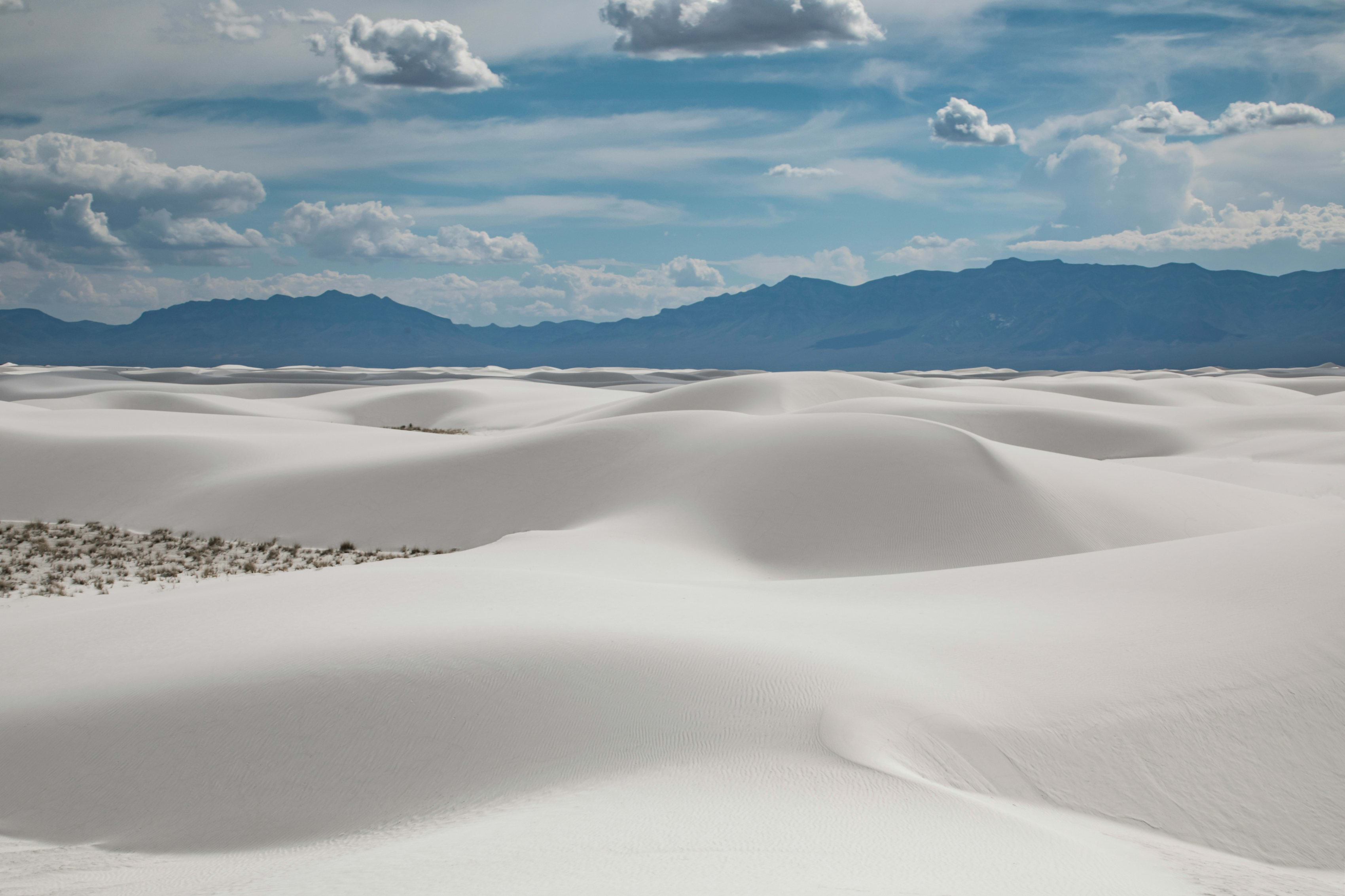 Sweeping view of White Sands National Park with wavy dunes and distant mountains under blue sky.