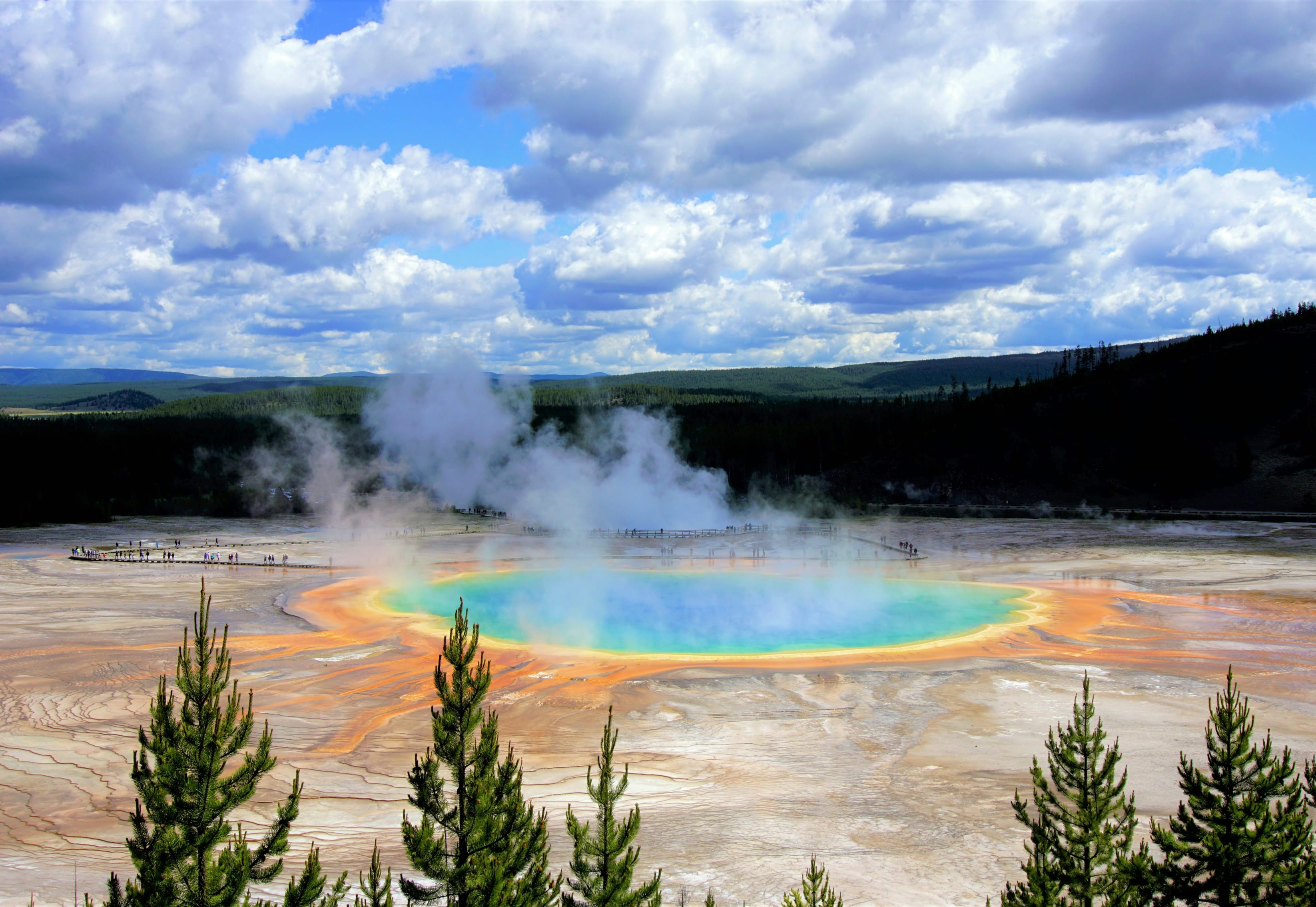 Grand Prismatic Spring with vibrant colors and steam at Yellowstone National Park under a cloudy sky.