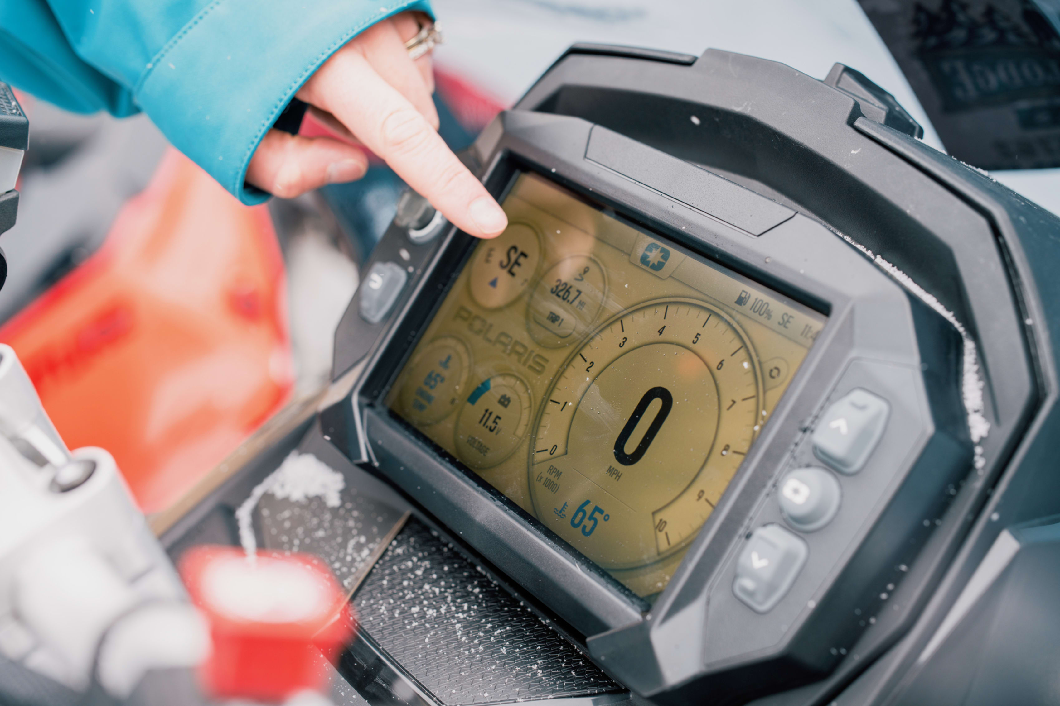A person points at a snowmobile screen displaying the Polaris Ride Command interface.