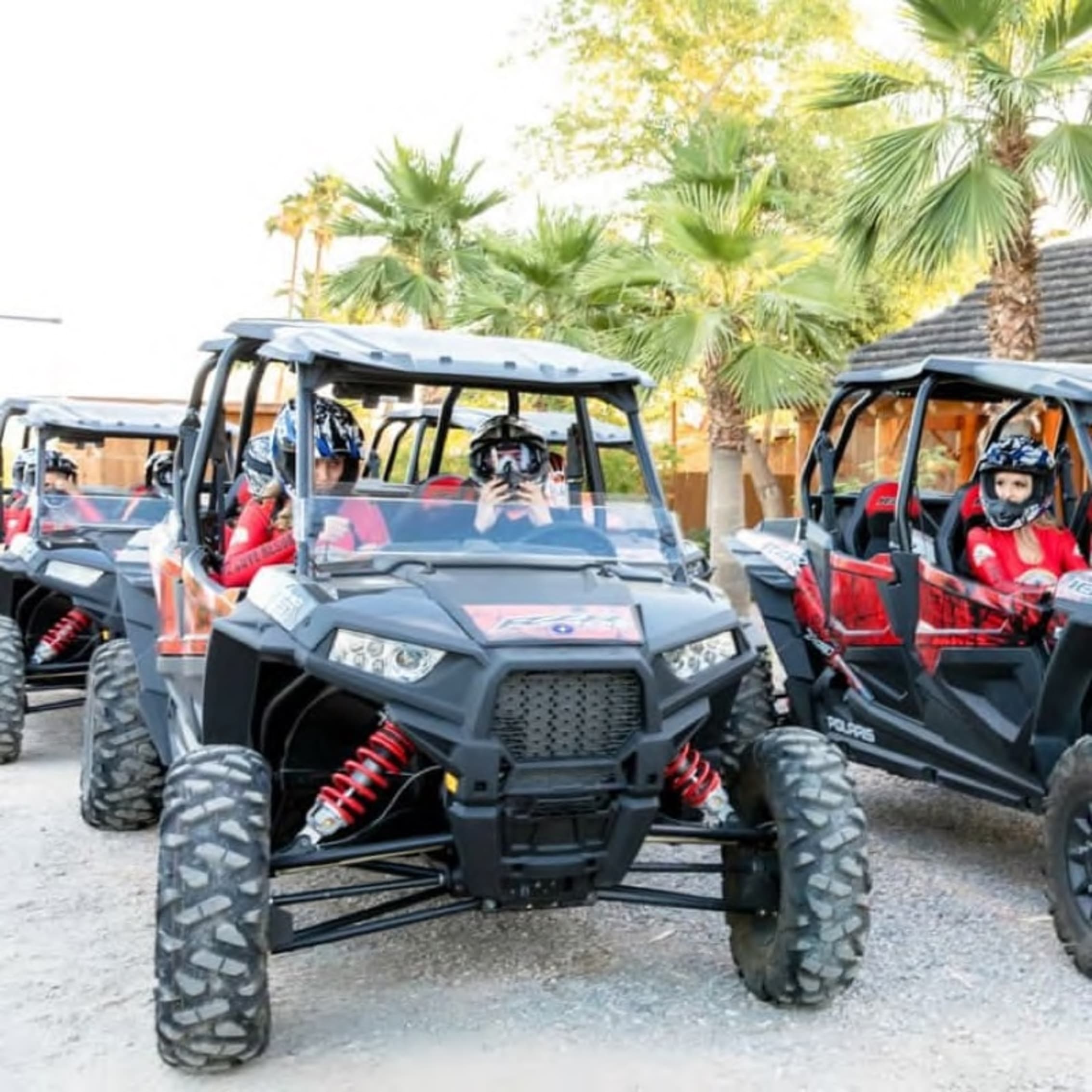 Drivers in protective gear seated in Polaris off-road vehicles, ready for an adventure.