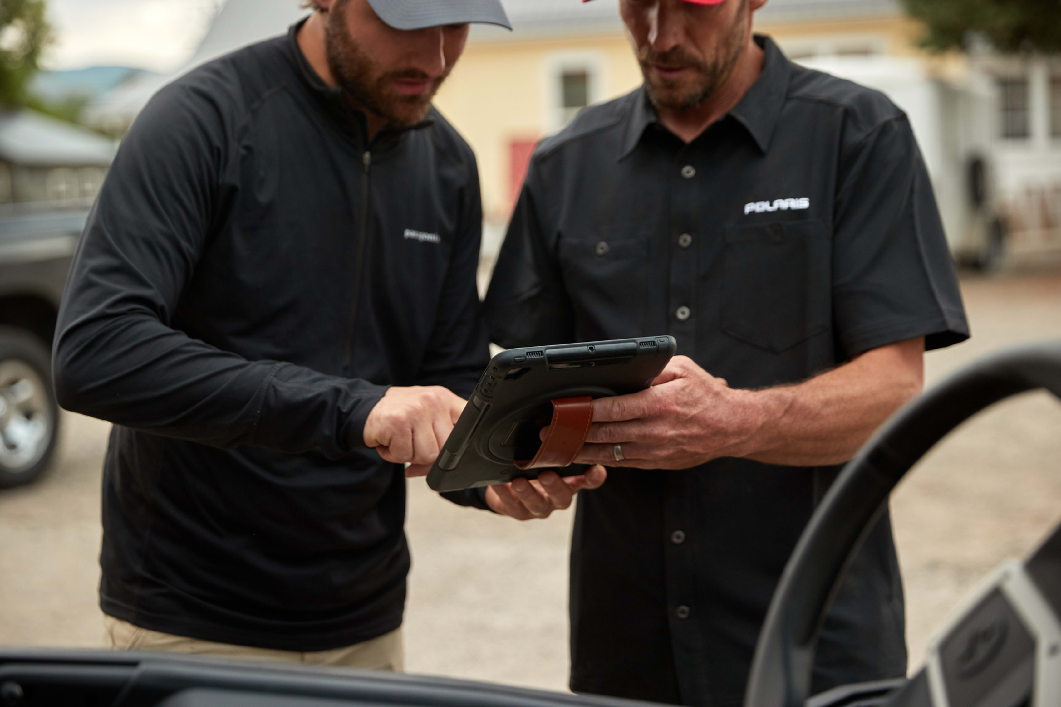 Two men interact with a ruggedized rental technology tablet..