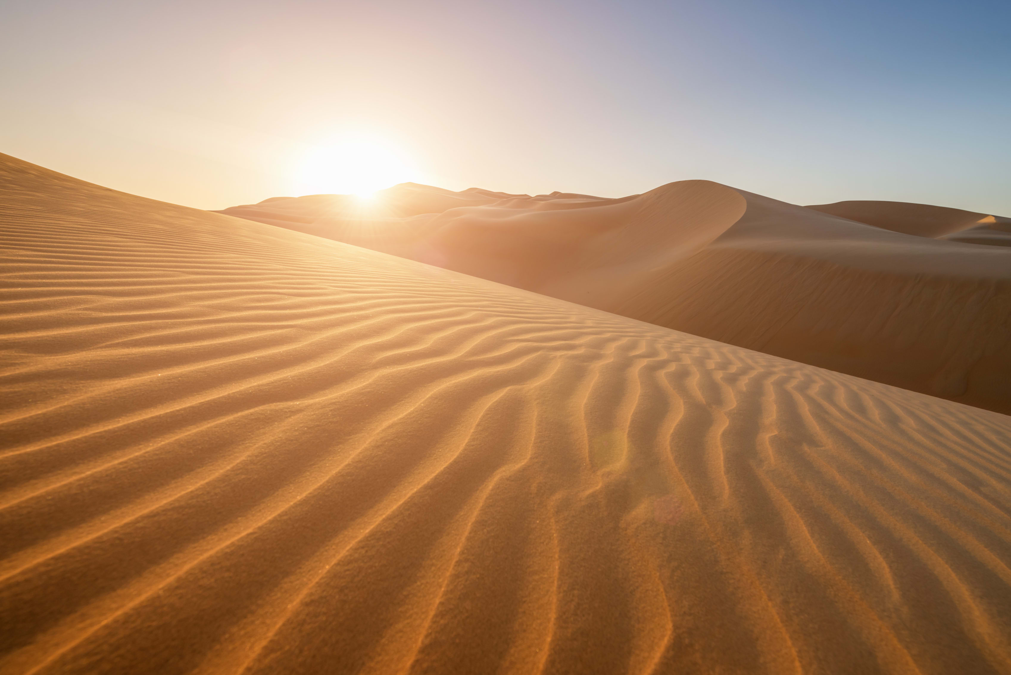 Golden sunrise over smooth sand dunes, casting shadows and textures on the sand
