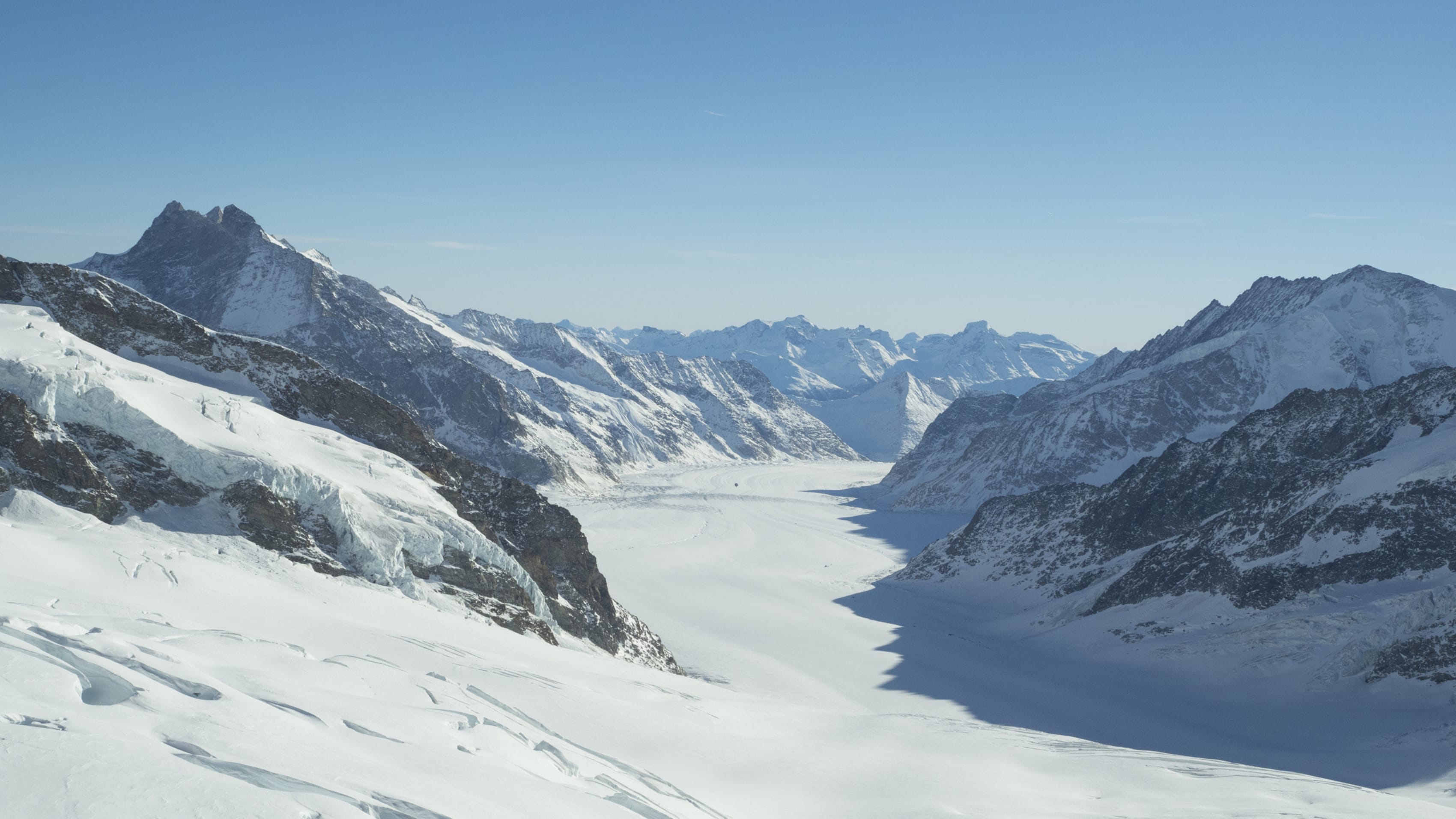Snowy mountain range with glacier under a clear sky.