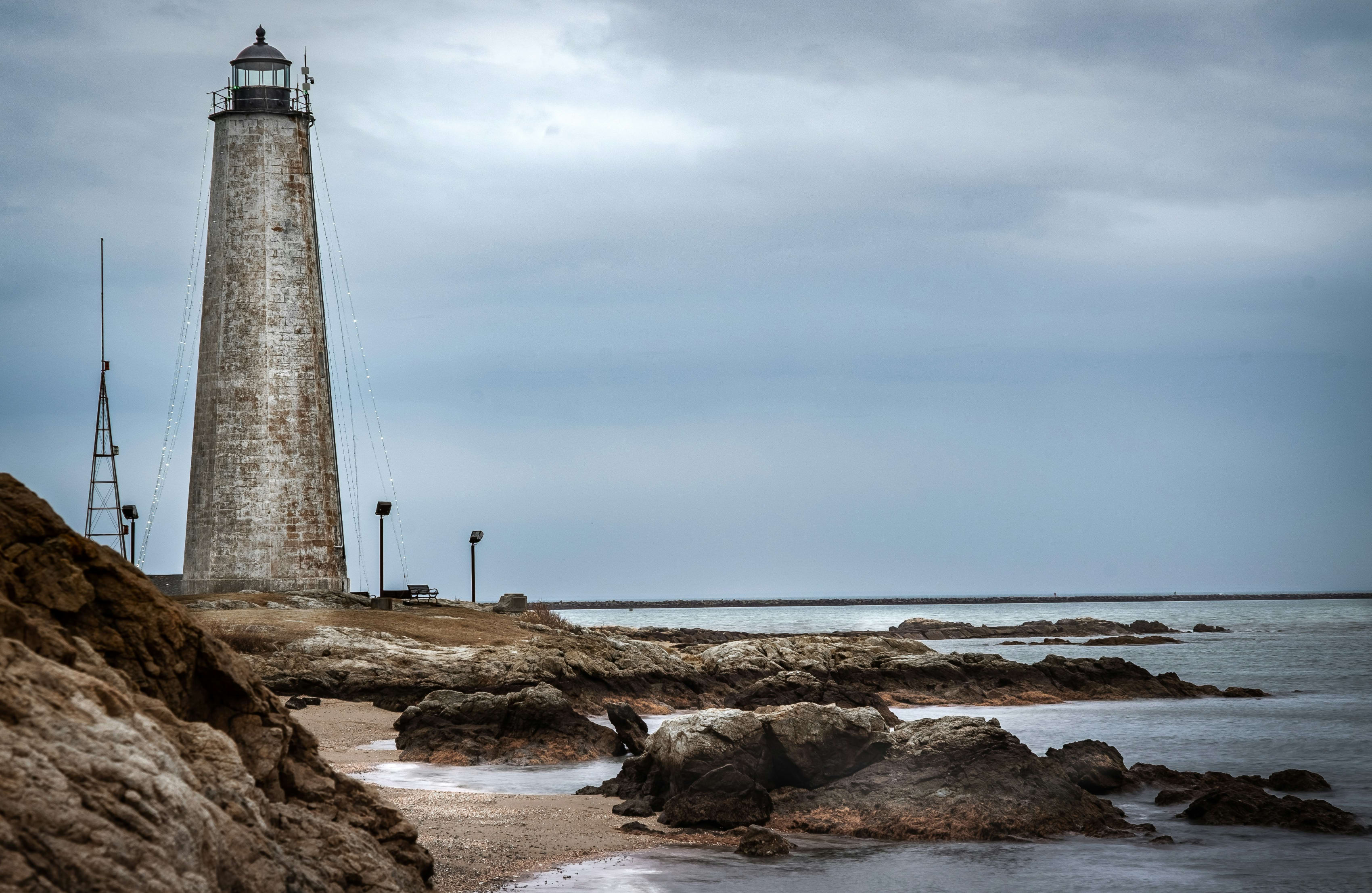 Historic lighthouse overlooking the sea along rocky Connecticut shoreline under a cloudy sky.