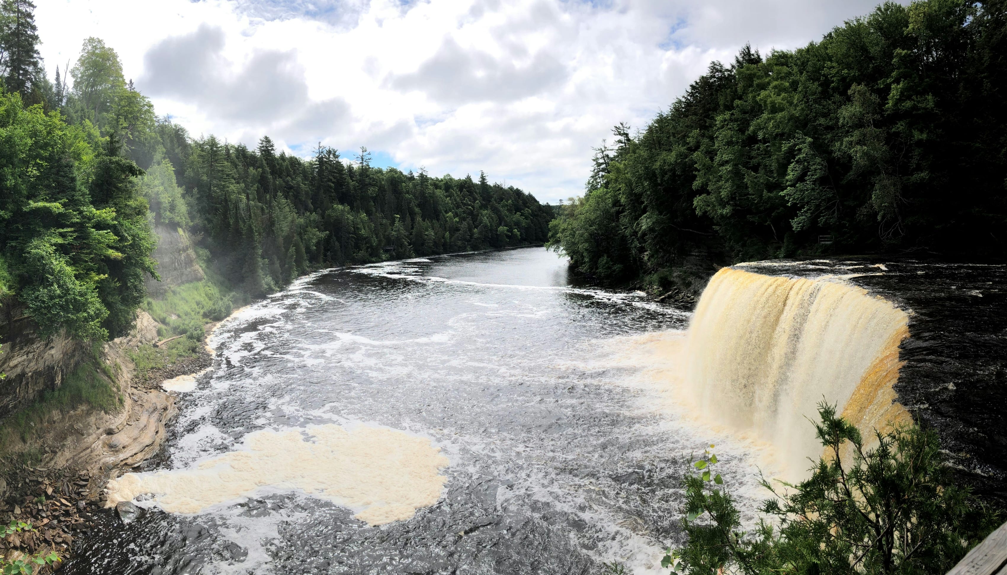 Panoramic view of a large waterfall in Michigan surrounded by lush forests on a cloudy day.