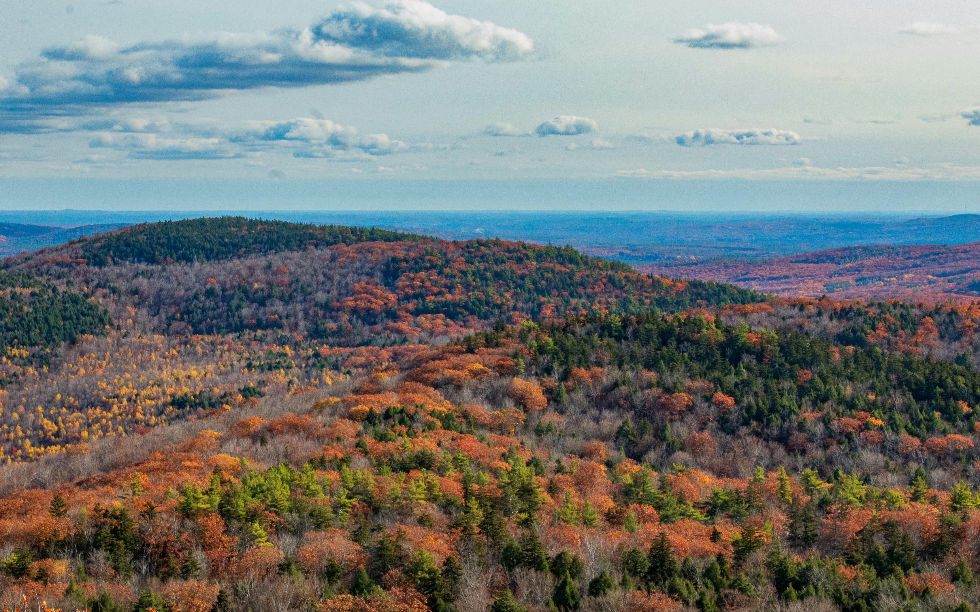 A scenic view of New Hampshire's autumn landscape with colorful foliage and rolling hills under a partly cloudy sky.
