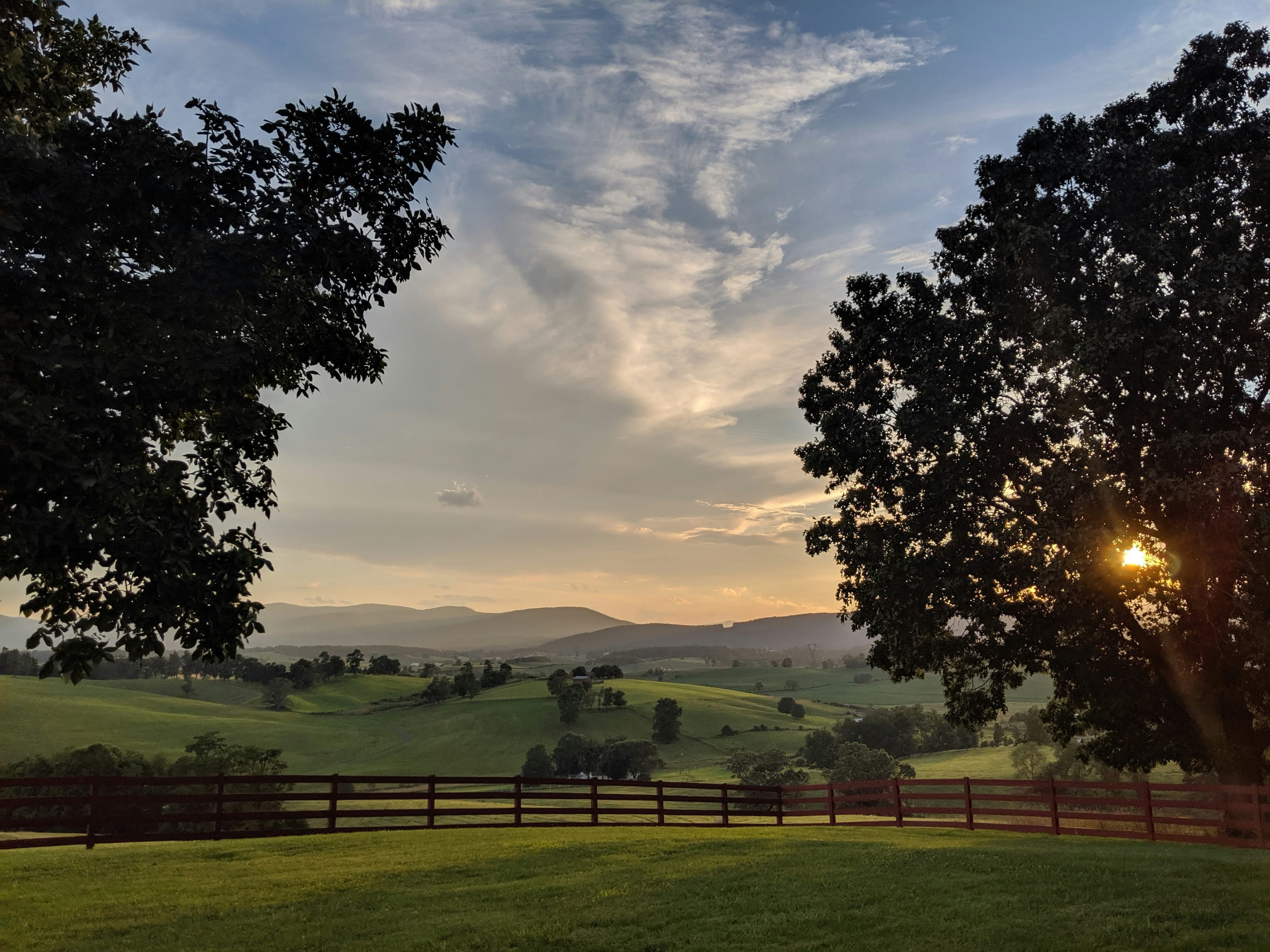 Sunset view over Virginia hills with a fence in the foreground and trees framing the serene landscape.