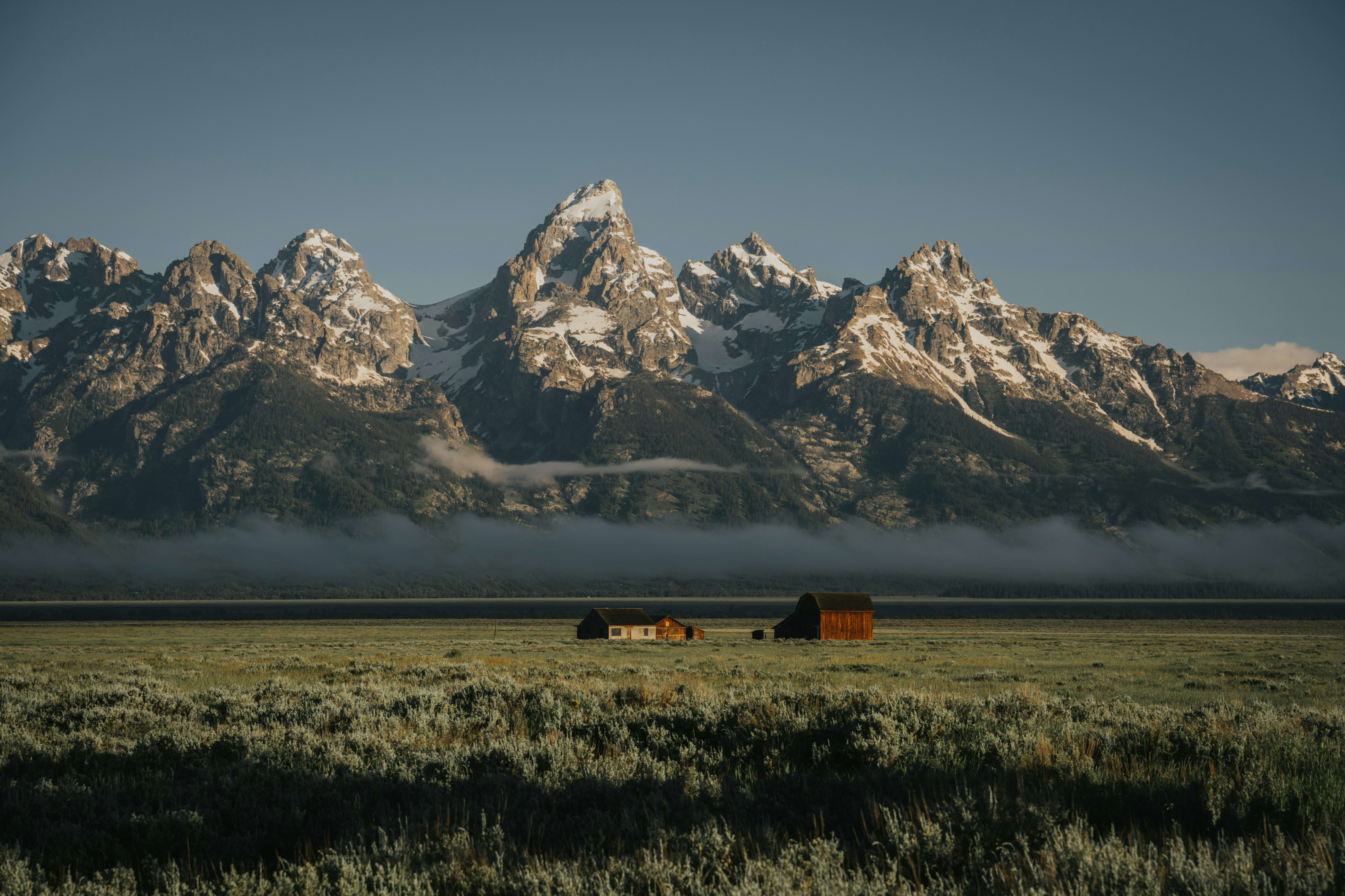 Scenic view of the Teton Range with snow-capped peaks and a low mist, with barns in the Wyoming valley.