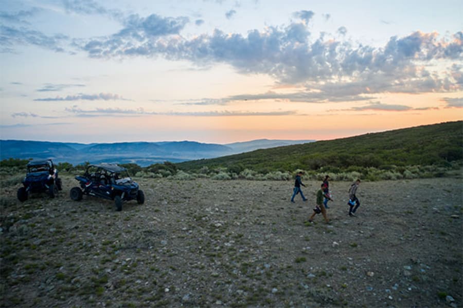 Group of riders at hilltop with UTVs at dusk