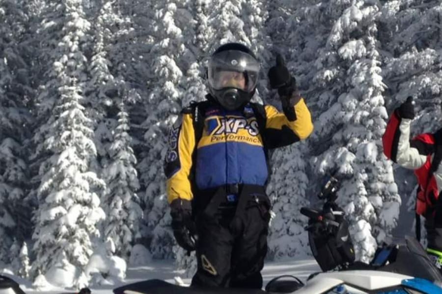 Three snowmobiles in front of snowy pines
