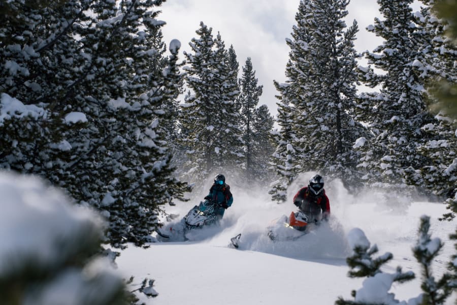 Two Polaris snowmobilers kicking up white powder