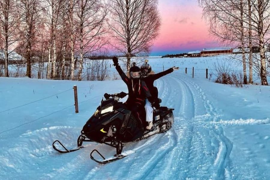 Two snowmobilers on trail at sunset