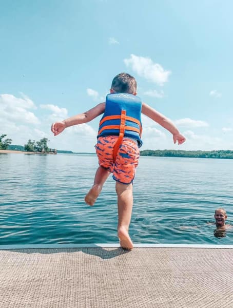 Young boy jumping into water off pontoon