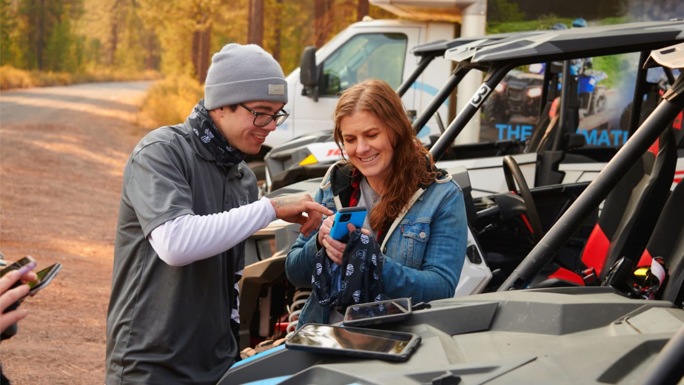 Guide assisting a happy adventurer with a mobile device before an off-road experience.