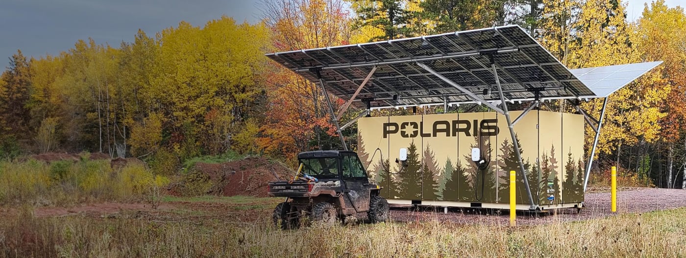 Polaris RANGER electric vehicle parked beside a solar charging station in a forest during autumn.