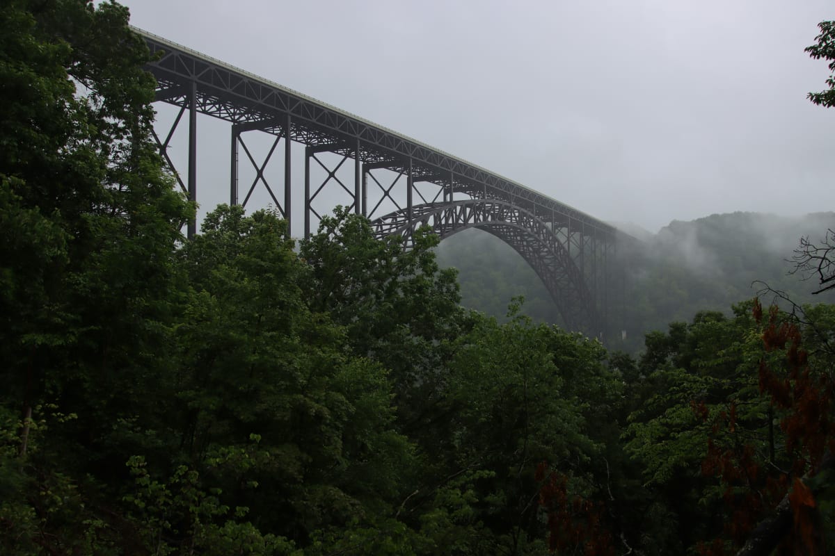 Misty view of the New River Gorge Bridge enveloped in fog with lush greenery surrounding it.