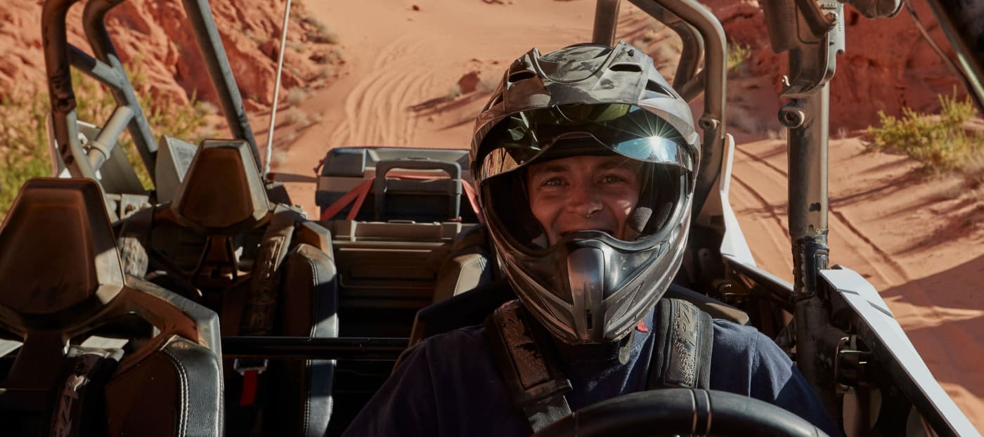Happy adventurer in a helmet, enjoying a desert ride in an off-road vehicle, embodying the thrill of an outfitter experience.