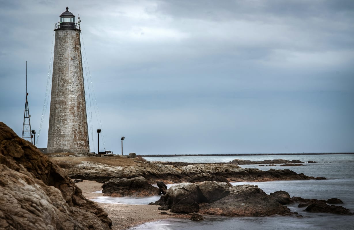 Historic lighthouse overlooking the sea along rocky Connecticut shoreline under a cloudy sky.