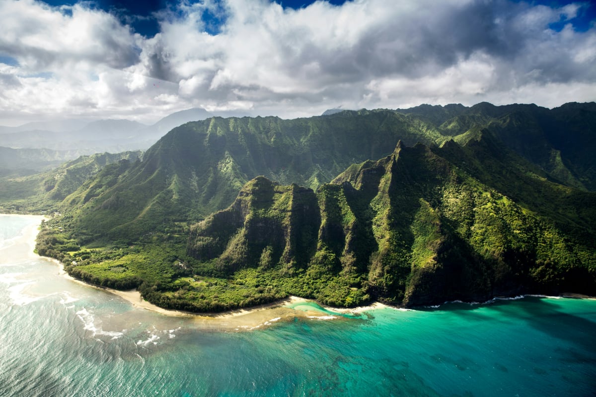Aerial view of Hawaii's lush green cliffs beside a turquoise sea, highlighting the natural beauty for adventure seekers.