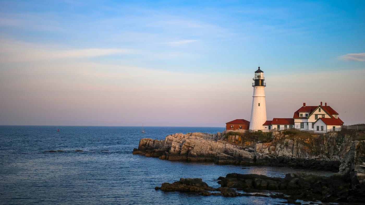 Historic Maine lighthouse during sunset with oceanfront and rocky coastline, inviting for tranquil adventure and exploration.