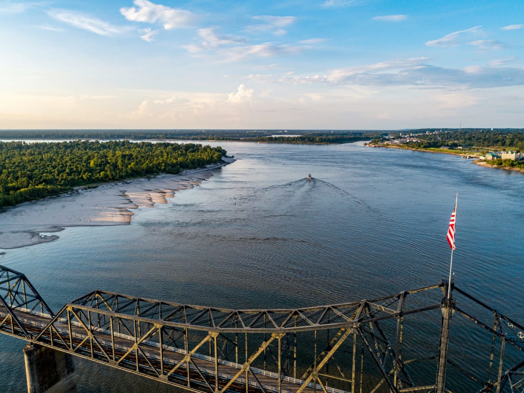 Aerial view of a large river in Mississippi with a bridge and American flag in the foreground.