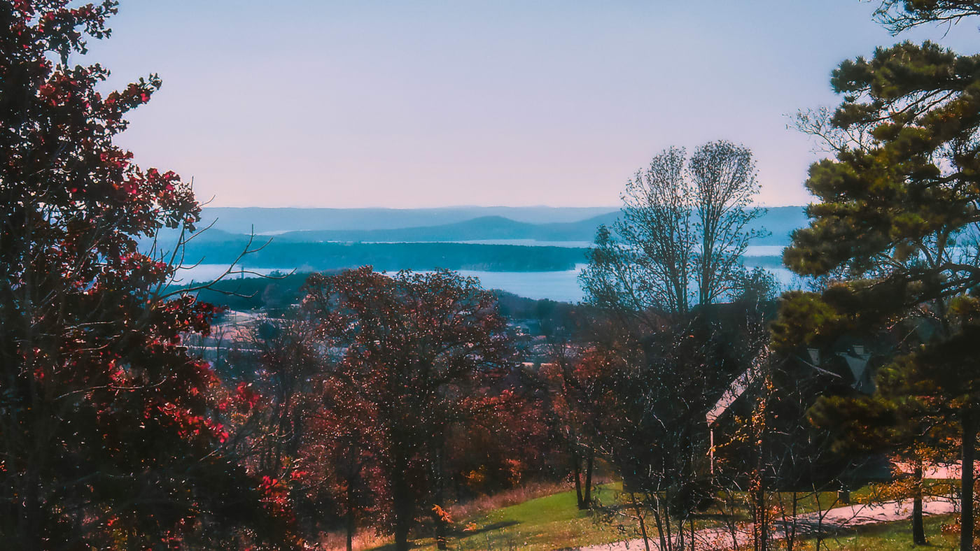 Scenic overlook of Missouri's landscape with vibrant autumn foliage and a view of distant hills across a serene lake.