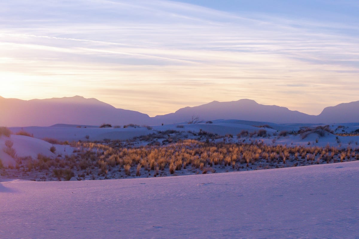 Sunset over the white dunes in New Mexico with purple mountains silhouette and soft sky gradient