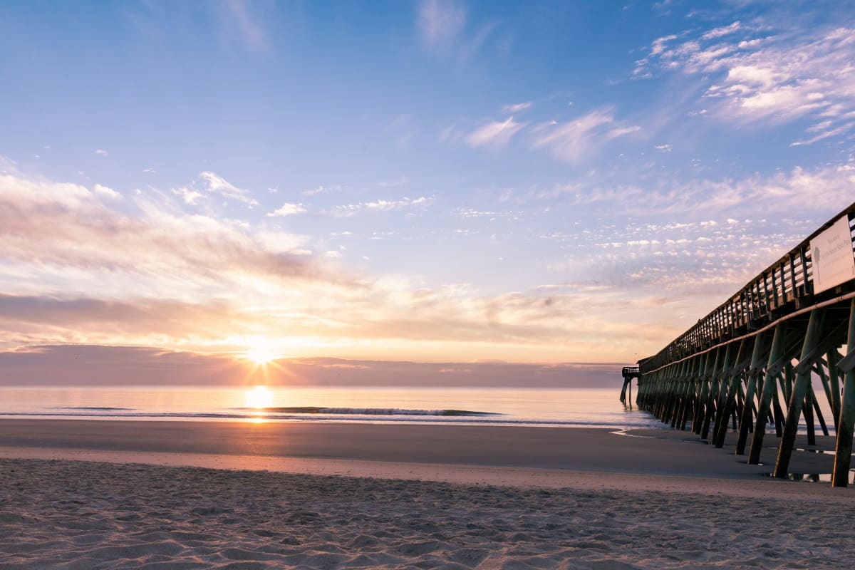 Sunrise at a South Carolina beach with a wooden pier extending into the water and a person admiring the view.