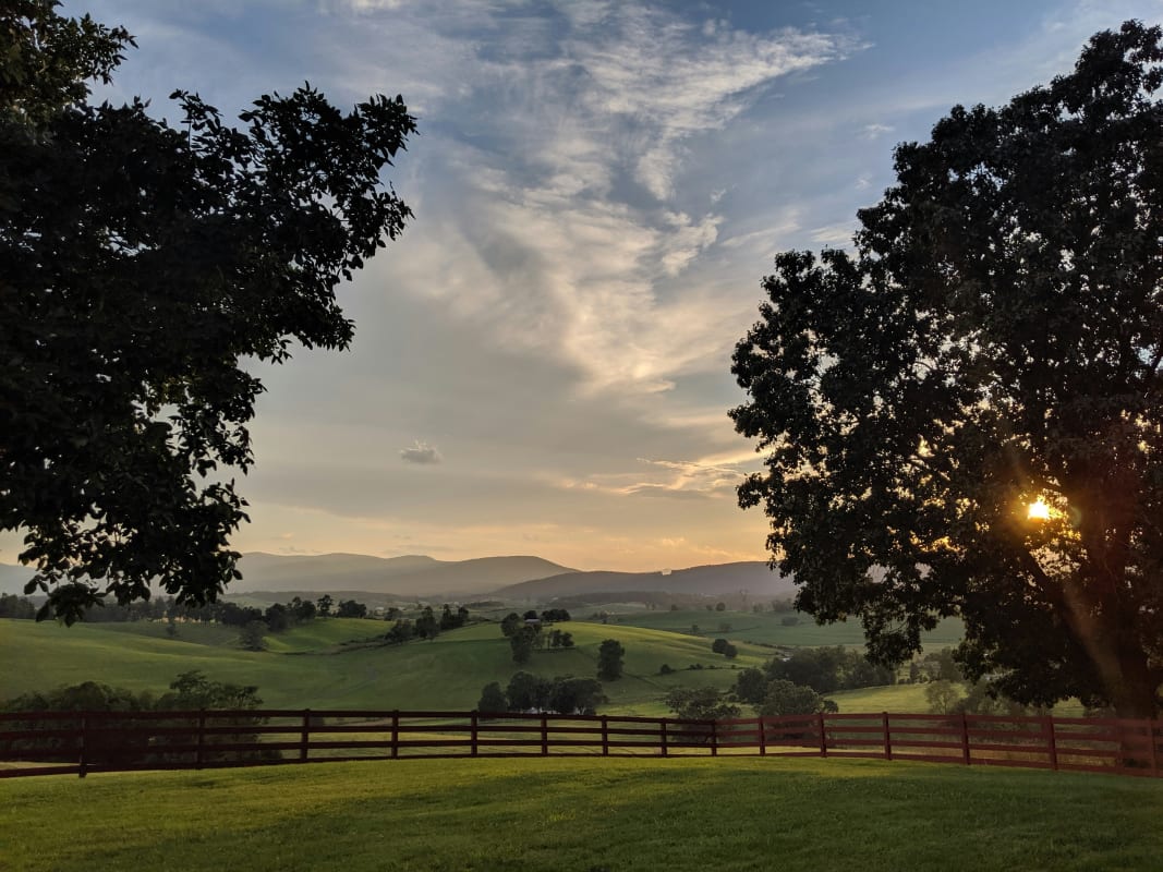 Sunset view over Virginia hills with a fence in the foreground and trees framing the serene landscape.