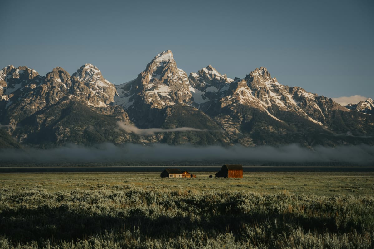 Scenic view of the Teton Range with snow-capped peaks and a low mist, with barns in the Wyoming valley.