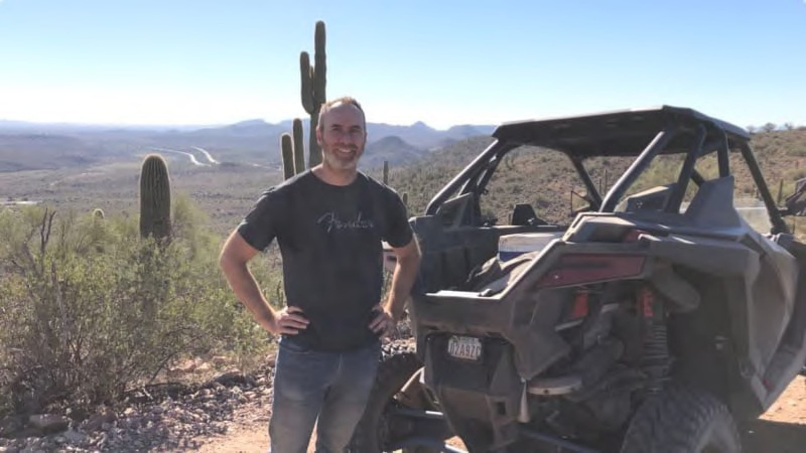 Happy adventurer posing with a Polaris off-road vehicle in a desert landscape with cacti, showcasing the excitement of outdoor exploration.