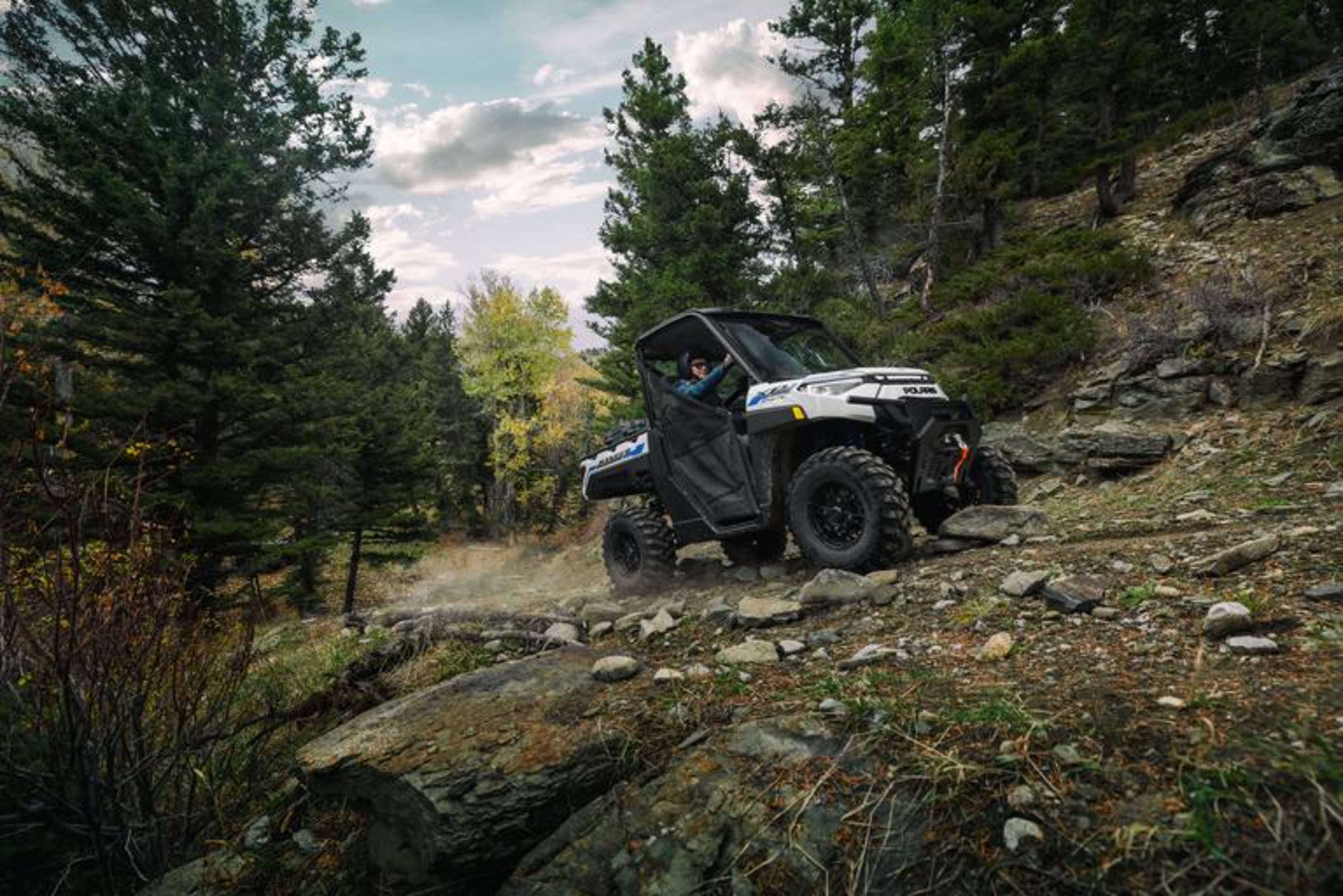 Polaris RANGER XP electric vehicle navigating a rocky, wooded trail with dust clouds in the air.