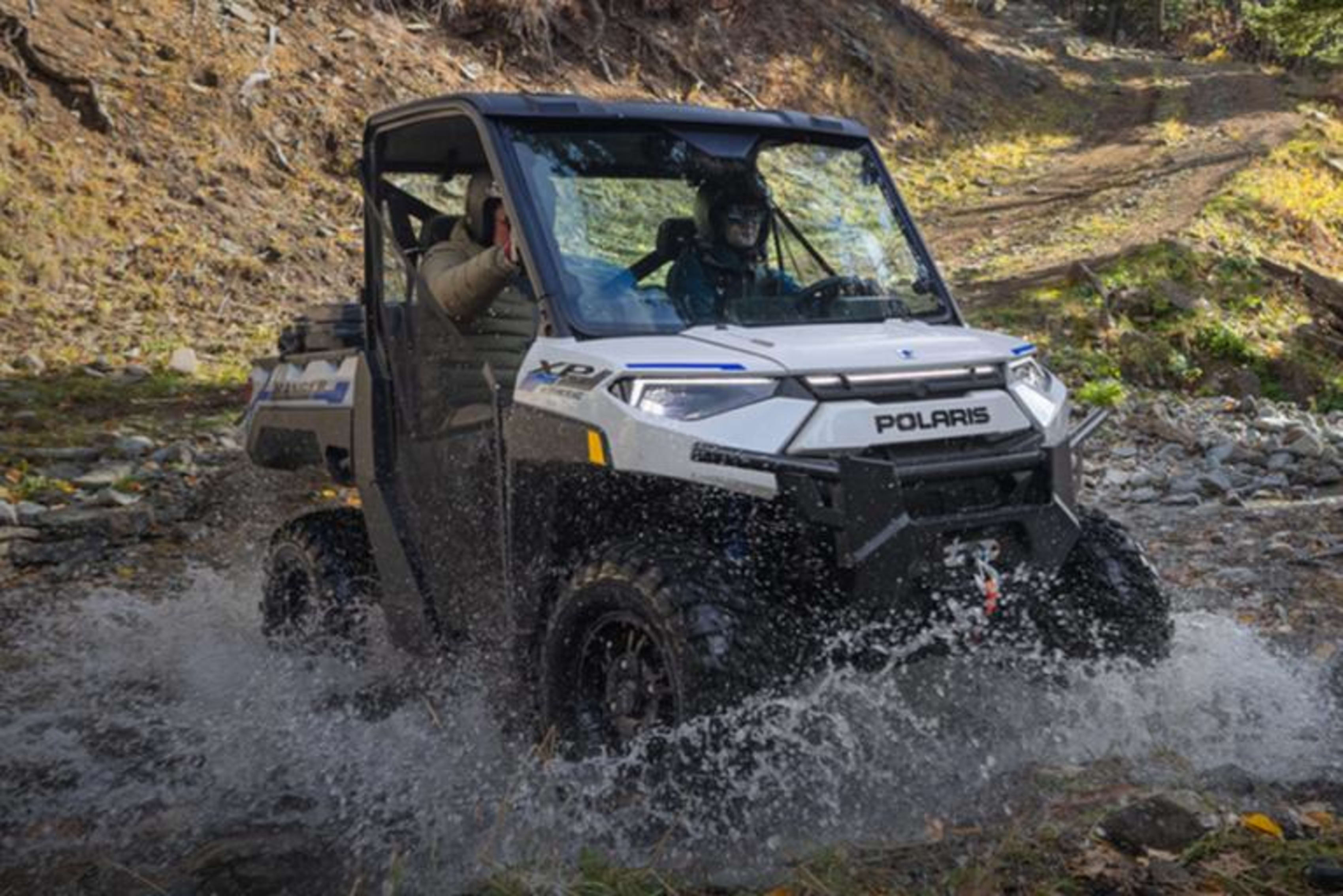 Polaris RANGER XP electric vehicle driving through a shallow river in a rugged, outdoor setting.