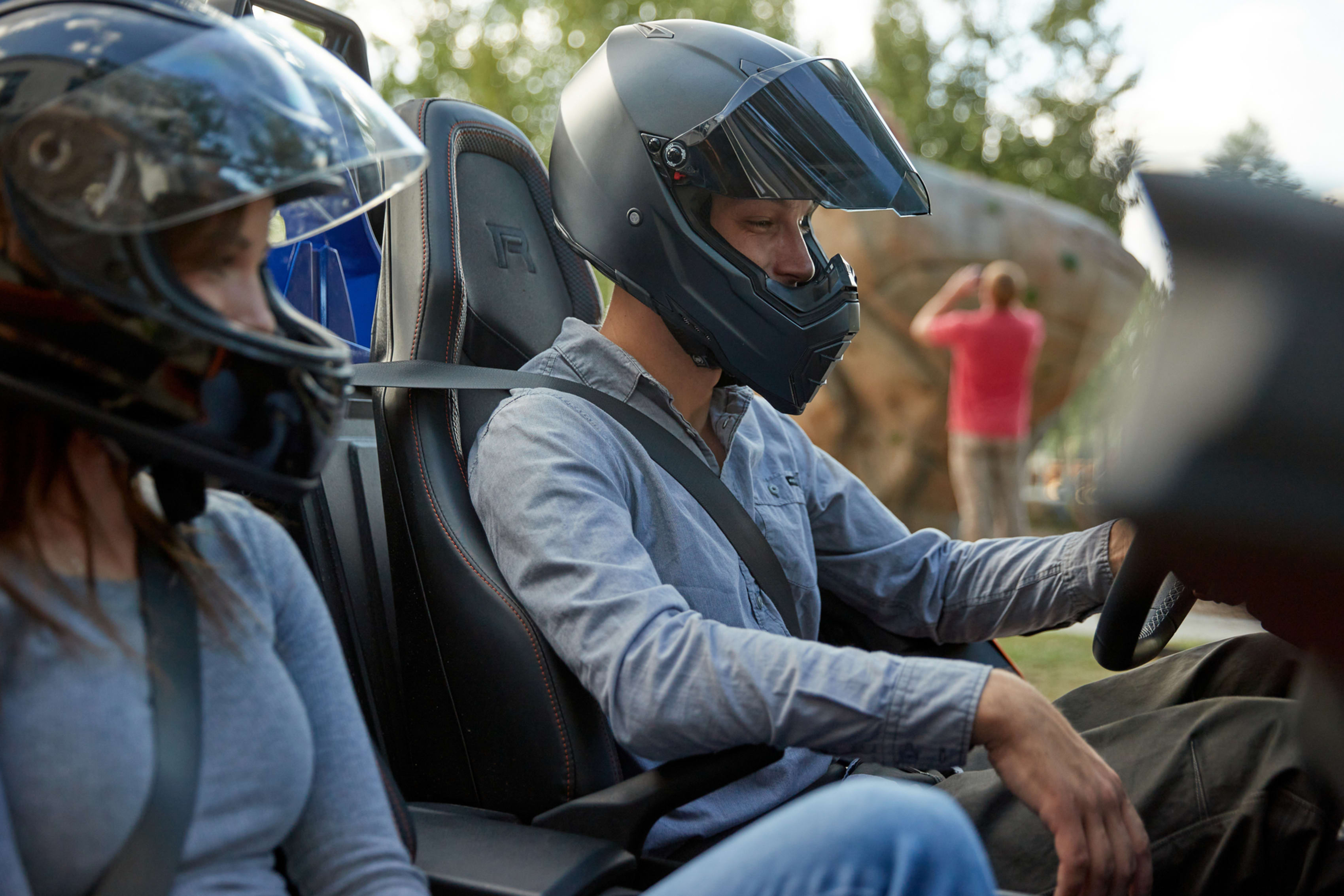 Two people wearing helmets taking a ride in an off-road vehicle, with trees in the background.