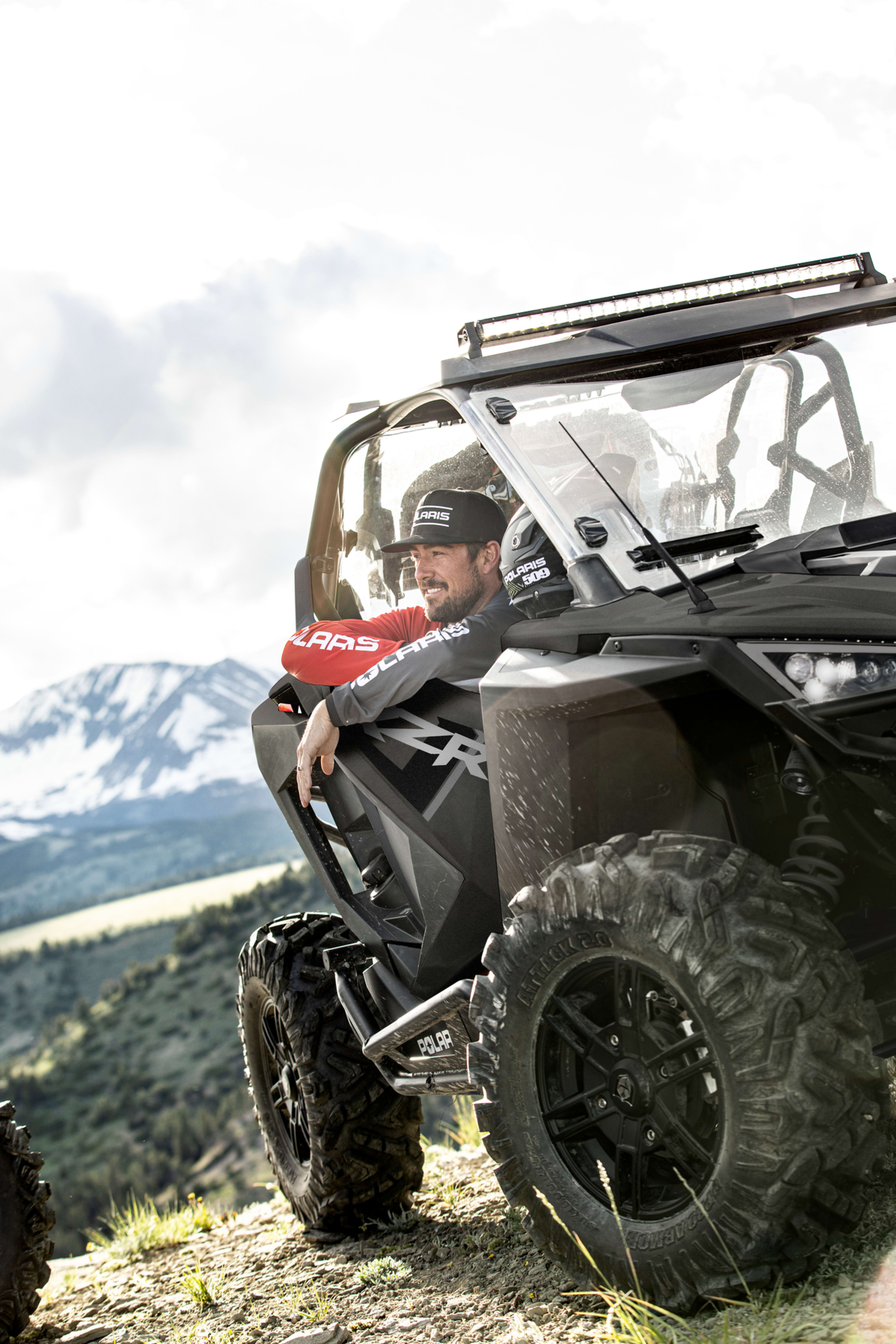 Confident man in a Polaris RZR with scenic mountainous backdrop, showcasing the vehicle's edge