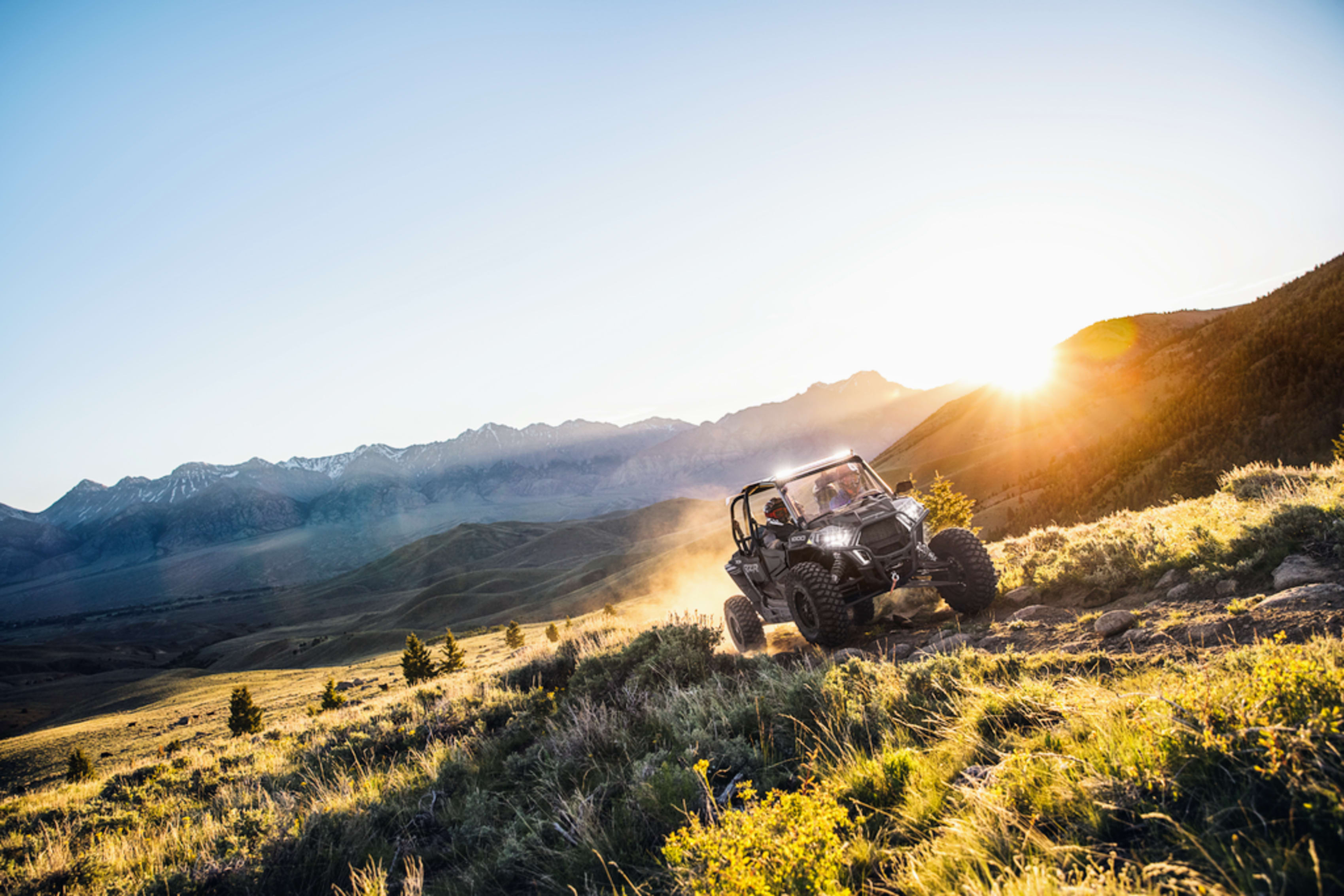 Four passengers in a Polaris side by side on a Wyoming trail at sunset
