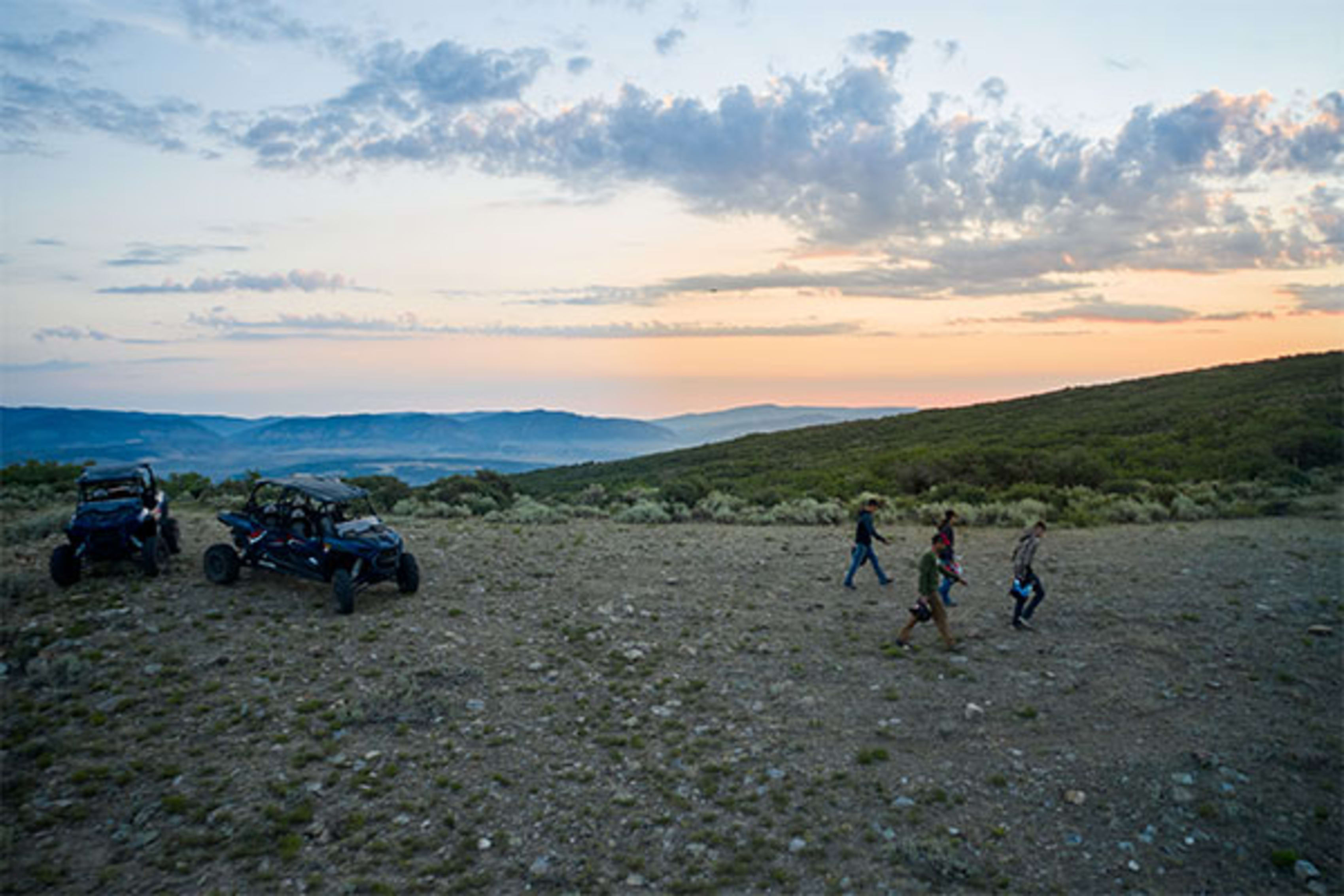 Group of riders at hilltop with UTVs at dusk