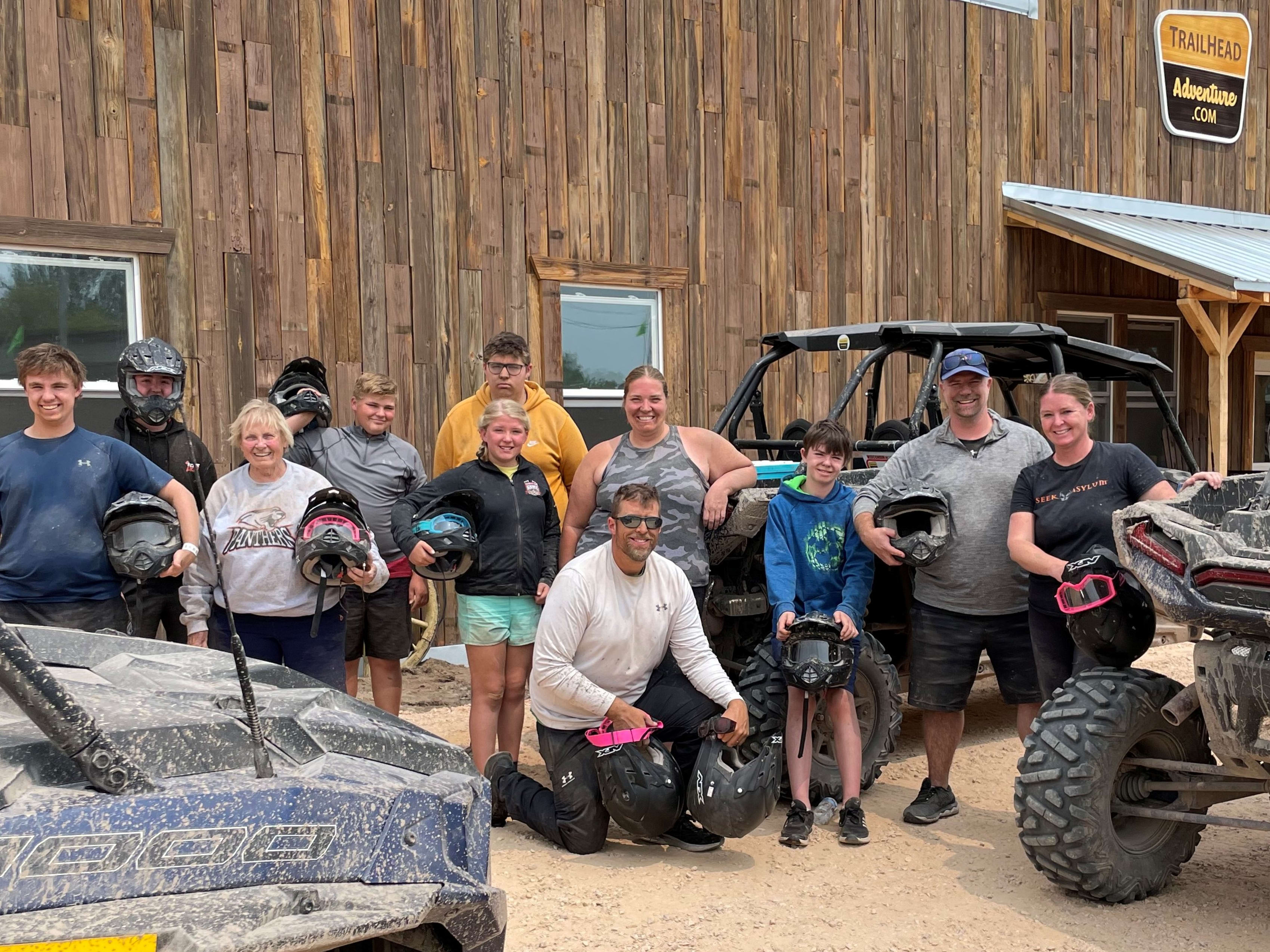 Large family group posing by muddy Polaris side by sides
