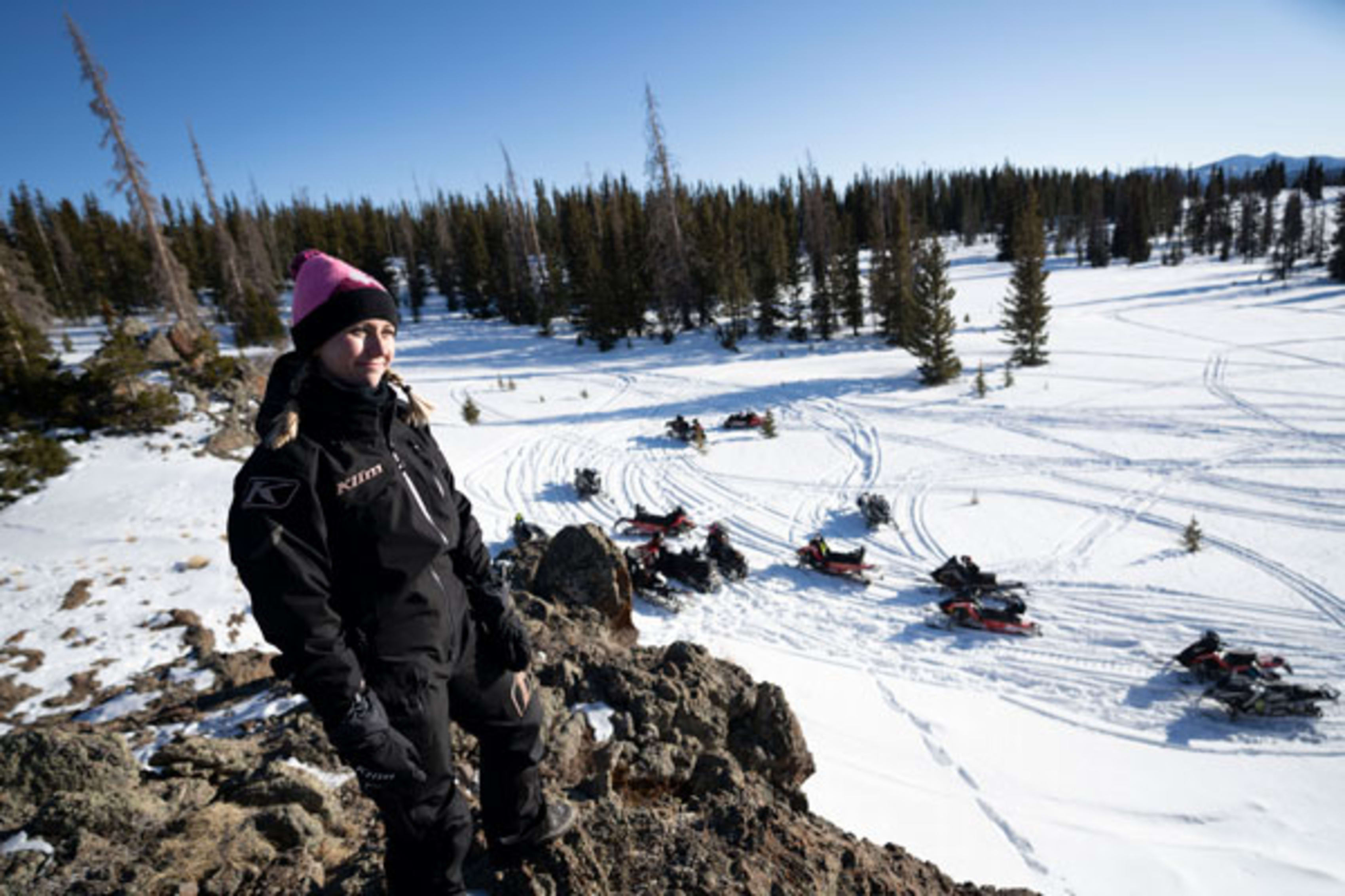 Woman standing on ridge above snowmobile gathering