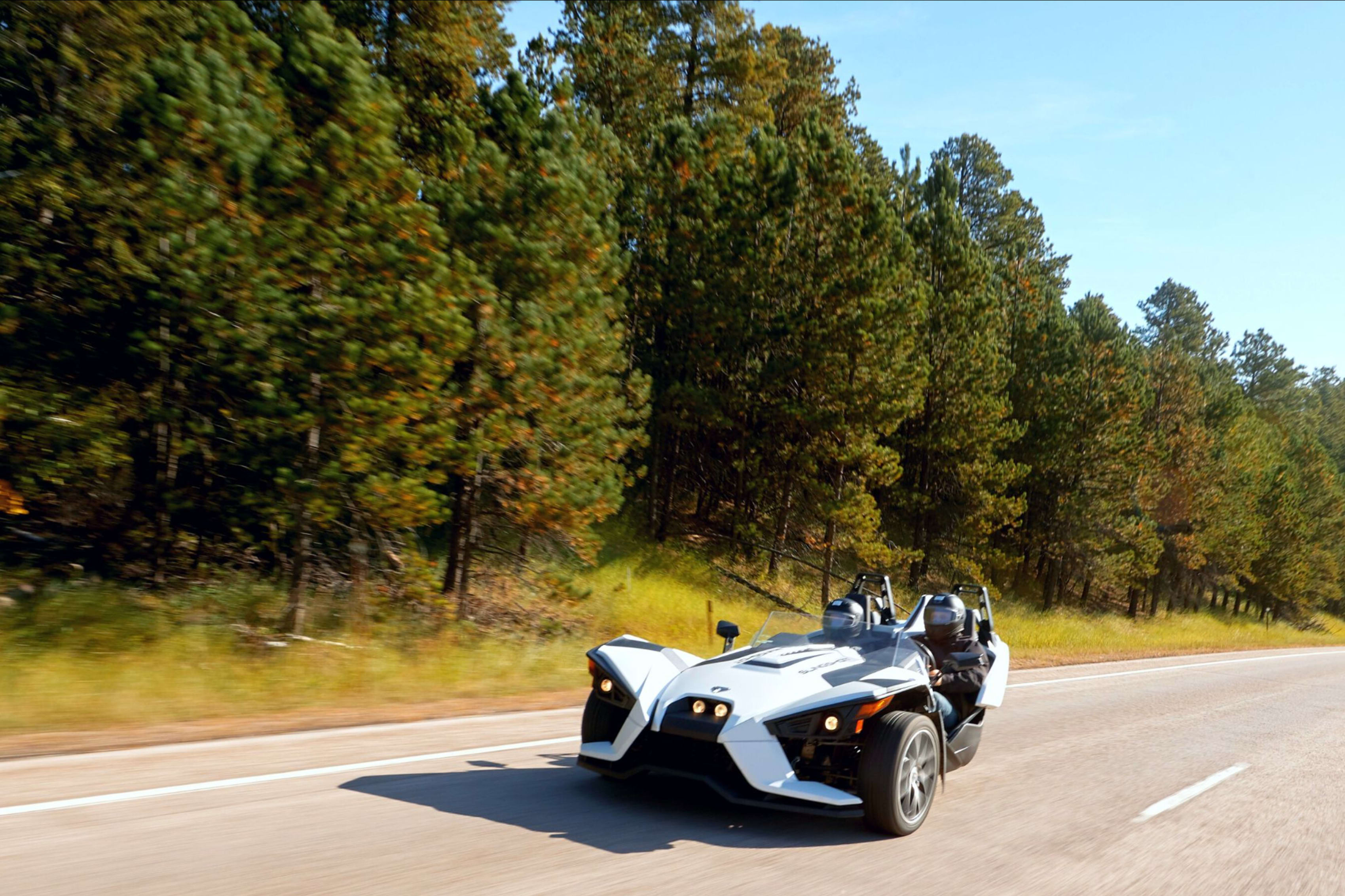 Two white Polaris Slingshots cruising on a highway